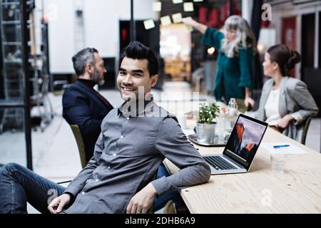 Ritratto di uomo d'affari sorridente seduto con i colleghi in riunione a. ufficio Foto Stock