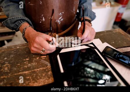 Sezione centrale del venditore senior che tiene occhiali da vista da tablet digitale e. telefono cellulare al banco cassa in hardware stor Foto Stock