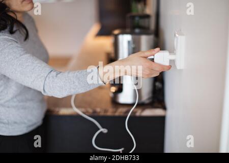 Sezione centrale della donna che collega il caricabatterie del telefono cellulare alla presa a muro casa Foto Stock