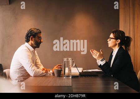 Vista laterale di avvocato femminile che spiega cliente maturo in riunione in ufficio Foto Stock