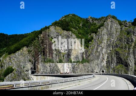 Strada Transfagarasan sopra la diga di Vidraru andando a due gallerie vicino alla costruzione di hydropower. Colline piene di rocce che illuminano alla luce del sole. Foto Stock