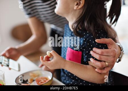 La metà della madre abbracciava la figlia mentre si serve la colazione a pranzo tabella Foto Stock