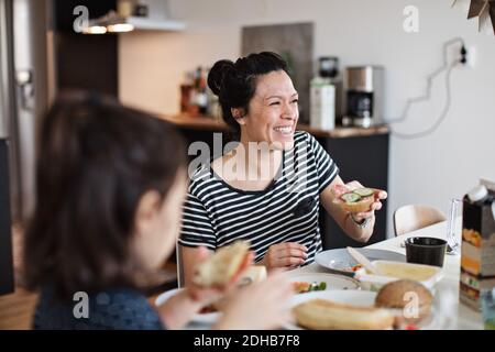 Madre sorridente seduta con la figlia mentre si serve la colazione a pranzo tabella Foto Stock