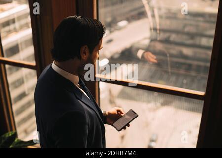 Vista ad alto angolo di un avvocato maschile con smartphone by finestra in ufficio Foto Stock