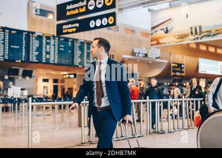 Uomo d'affari maturo con i bagagli a piedi nel terminal dell'aeroporto Foto Stock