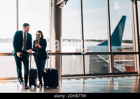 Tutta la lunghezza della coppia di lavoro con bagaglio utilizzando il telefono cellulare in aeroporto Foto Stock