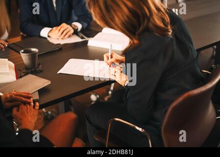 Avvocato donna che firma documenti mentre siede in riunione con i colleghi in ufficio Foto Stock