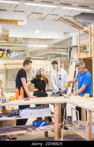 Falegname maschio che spiega la trivella elettrica ai partecipanti al banco di lavoro durante formazione Foto Stock