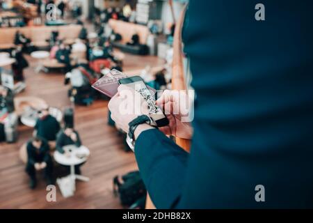 Immagine ritagliata di uomo d'affari che tiene il telefono cellulare e passaporto in aeroporto Foto Stock