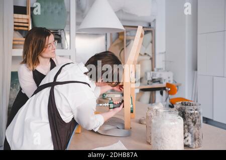 Lavoratrice di tappezzeria femminile che usa la pistola a graffetta sulla sedia in officina Foto Stock