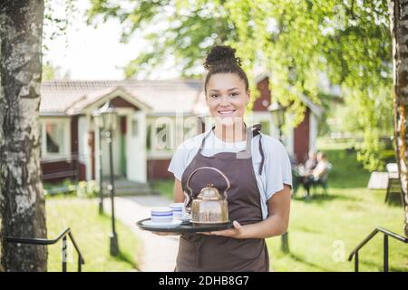 Ritratto della giovane cameriera sorridente che tiene il vassoio di servizio al ristorante Foto Stock