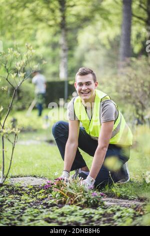 Ritratto a lunghezza intera di giovane uomo sorridente che piantava in giardino Foto Stock