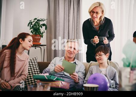 Nonno con compleanno presenta lettura biglietto d'auguri per la famiglia in soggiorno Foto Stock