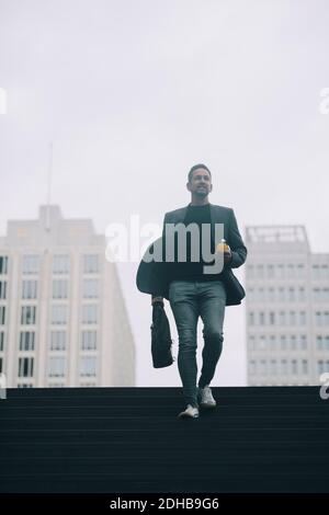 Uomo d'affari che si muove su gradini alla metropolitana contro il cielo chiaro Foto Stock