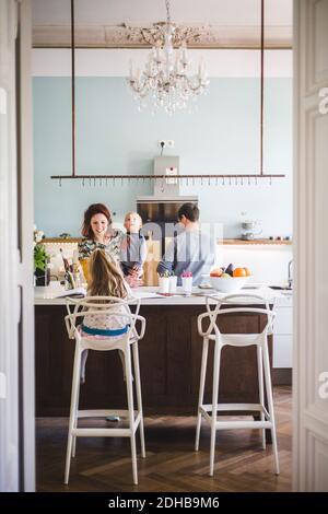 Donna sorridente che porta il figlio mentre guarda la ragazza che studia dentro cucina a casa Foto Stock