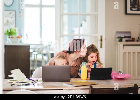 Donna mid adulta che bacia la figlia mentre si siede con il figlio a. casa Foto Stock