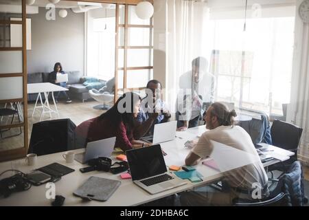 Colleghi di sesso maschile e femminile che discutono in riunione presso l'ufficio creativo vista attraverso la parete di vetro Foto Stock