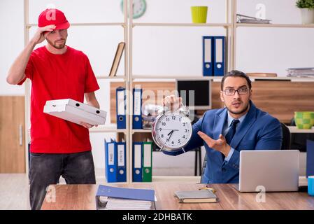 Giovane uomo che consegna la pizza in ufficio in gestione del tempo conc Foto Stock