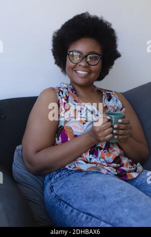 Sezione centrale della donna afroamericana seduta sul divano bere tazza di caffè. Auto isolamento a casa durante la covid coronavirus 19 pandemia. Foto Stock