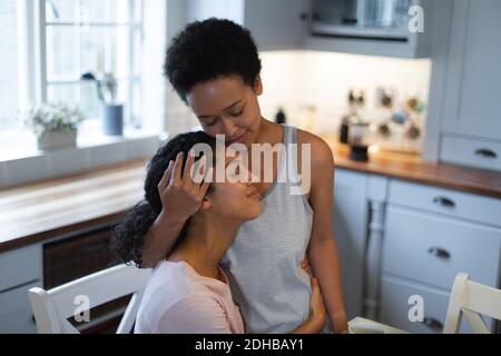 Felice misto razza coppia femminile abbracciare in cucina al mattino. Auto isolamento qualità tempo a casa insieme durante coronavirus covid 19 pandemia. Foto Stock