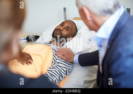 Giovane uomo che guarda la famiglia mentre si sdraiò a letto a. ospedale Foto Stock