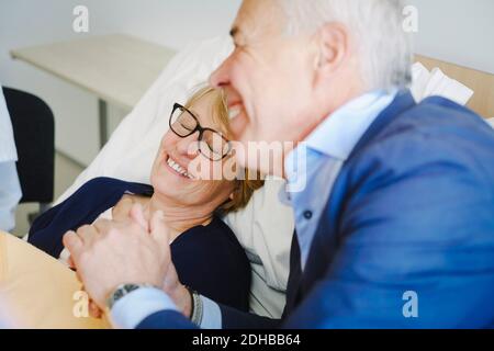 Donna sorridente con gli occhi chiusi dal partner senior in ospedale reparto Foto Stock