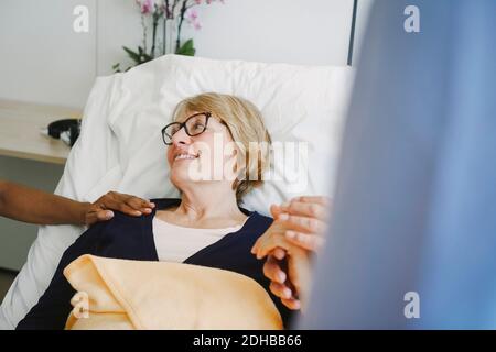 Donna anziana che guarda il medico incoraggiante mentre tiene le mani del socio in reparto all'ospedale Foto Stock