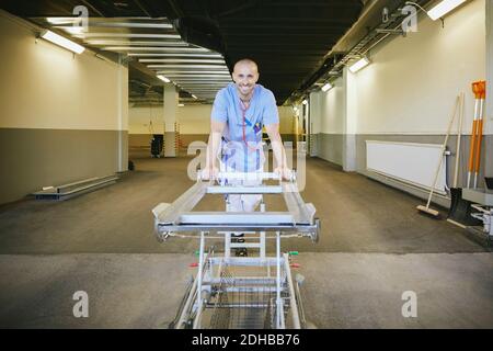Sorridente medico maschile in piedi con barella nel corridoio ospedaliero Foto Stock