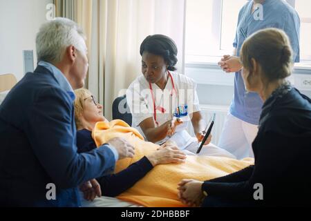 Dottore con infermiera che spiega paziente maturo e i suoi amici a. reparto ospedaliero Foto Stock