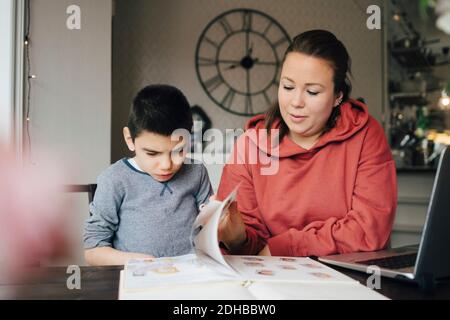 Madre che legge storia da libro dell'immagine per il figlio autistico mentre seduto a casa Foto Stock