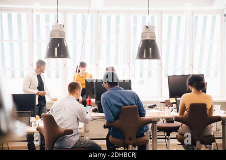 I progettisti di software maschili e femminili discutono alla scrivania contro la finestra in ufficio creativo Foto Stock