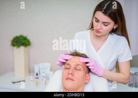 Cosmetici maschili. Un uomo dall'aspetto bello che riceve un trattamento viso presso una lussuosa spa Foto Stock