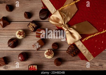 Cioccolatini assortiti in elegante confezione regalo rossa con nastro dorato posto su un tavolo di legno. Un'elegante opzione regalo di natale e giorno di valentines con Foto Stock