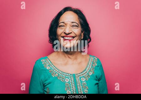 Ritratto di donna anziana sorridente che indossa salwar kameez contro il rosa sfondo Foto Stock