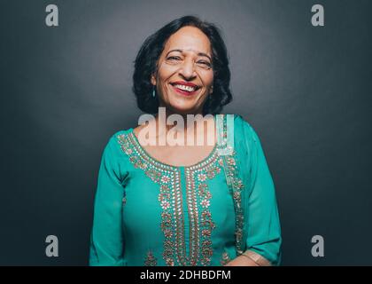 Ritratto di sorridente donna anziana che indossa salwar kameez contro grigio sfondo Foto Stock