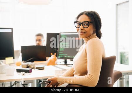 Ritratto di una programmatore femminile seduto alla scrivania con la collega in background in ufficio creativo Foto Stock