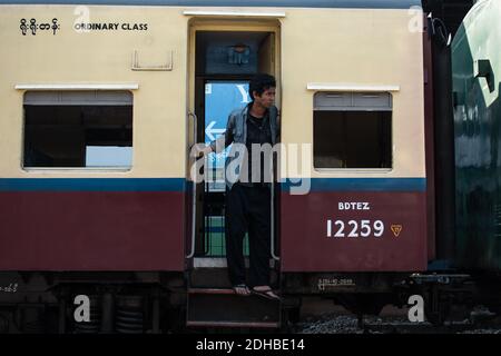 Yangon, Myanmar - 31 dicembre 2019: Un uomo birmano locale in piedi nella porta di apertura in classe ordinaria del treno circolare tradizionale alla ferrovia Foto Stock