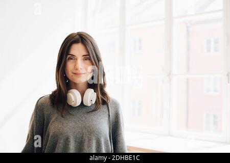 Ritratto del programmatore di computer femminile con le cuffie in piedi contro la finestra in ufficio Foto Stock