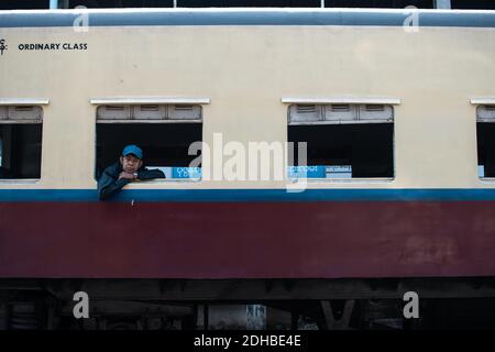 Yangon, Myanmar - 31 dicembre 2019: Un uomo birmano locale con un cappello che pende da una finestra in classe ordinaria del treno circolare tradizionale alla ferrovia Foto Stock