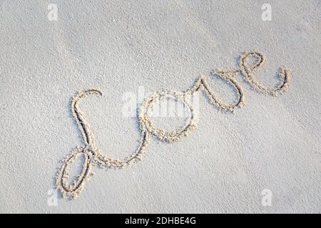 Mano che scrive amore sulla sabbia con spazio di copia. Romantico modello di spiaggia, parola d'amore su sfondo di sabbia, look 3D. Foto Stock