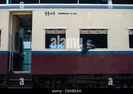 Yangon, Myanmar - 31 dicembre 2019: Un uomo birmano locale con un cappello che pende da una finestra in classe ordinaria del treno circolare tradizionale alla ferrovia Foto Stock