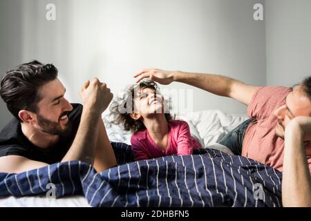 I padri che giocano con la figlia allegra mentre si sdraia sul letto a. casa Foto Stock