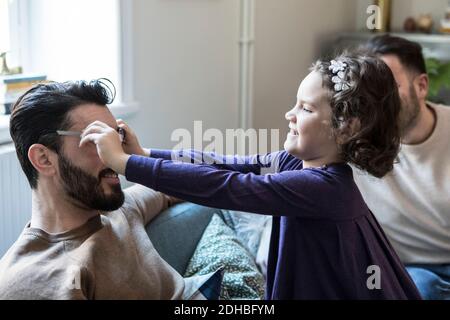 Figlia che fa il padre indossare gli occhiali mentre si siede sul divano a. casa Foto Stock