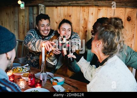 Felice uomo e amici che tostano le bottiglie di birra mentre si siede cabina di tronchi Foto Stock