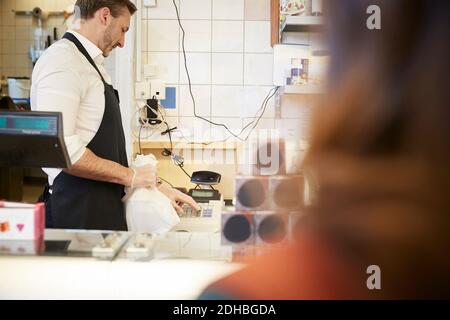 Cassiere maschile che tiene in mano una borsa di plastica mentre si utilizza il registratore di cassa negozio Foto Stock