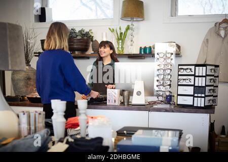 Il proprietario sorridente che parla con il cliente femminile mentre riceve il pagamento a. banco cassa in negozio Foto Stock