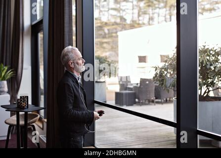 Uomo d'affari anziano che ascolta la musica mentre si alza dalla finestra in ufficio Foto Stock