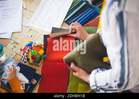 Vista ad alto angolo del designer di moda che sceglie tessuti dai colori swatch mentre la bambina gioca con il tessuto immagine bo Foto Stock