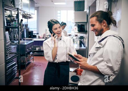 Chef di sesso maschile e femminile che utilizzano telefoni cordless e tablet digitali in cucina Foto Stock