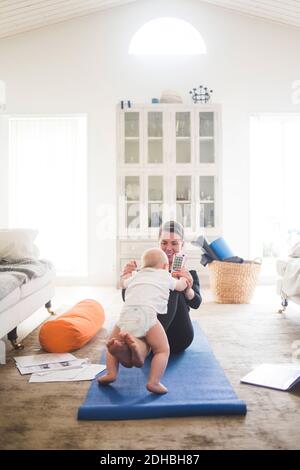 Felice madre che gioca con la figlia mentre si siede sul tappetino per esercizi in ufficio a casa Foto Stock
